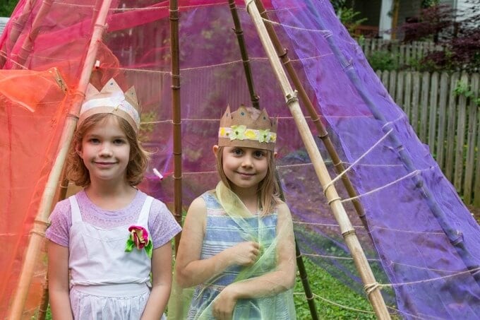 Two kids wearing their new handmade flower crowns and ready for pretend play in a backyard teepee.
