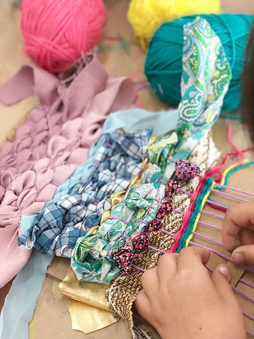 Student weaving yarn and ribbon on cardboard loom