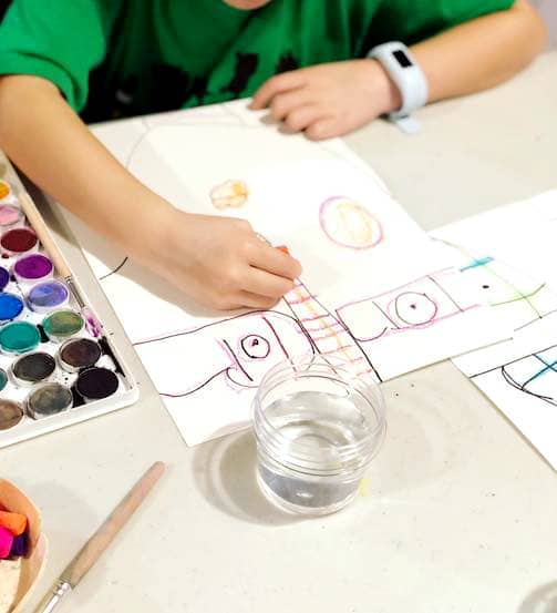 Child drawing portrait on paper with oil pastels