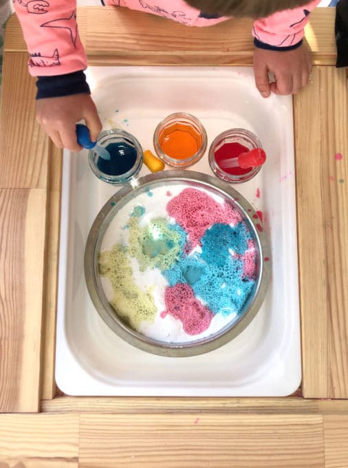 Child squeezing pipettes with colored vinegar and baking soda in tray
