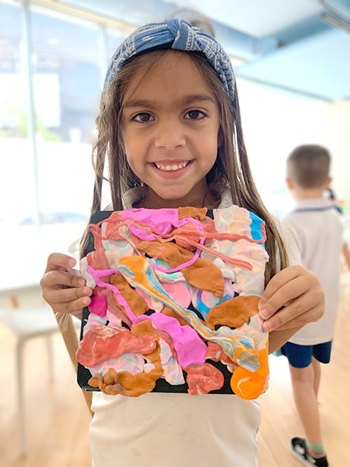 Child holding up colored air dry clay painting