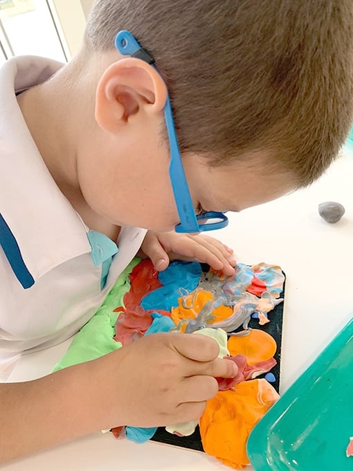 Child pressing colored air dry clay onto wooden board