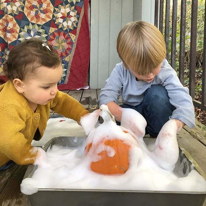 Two children playing with pumpkin and foamy soap – fun fall sensory play for babies.