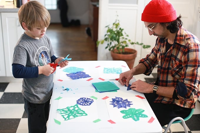 boy and parent cutting paper snowflakes