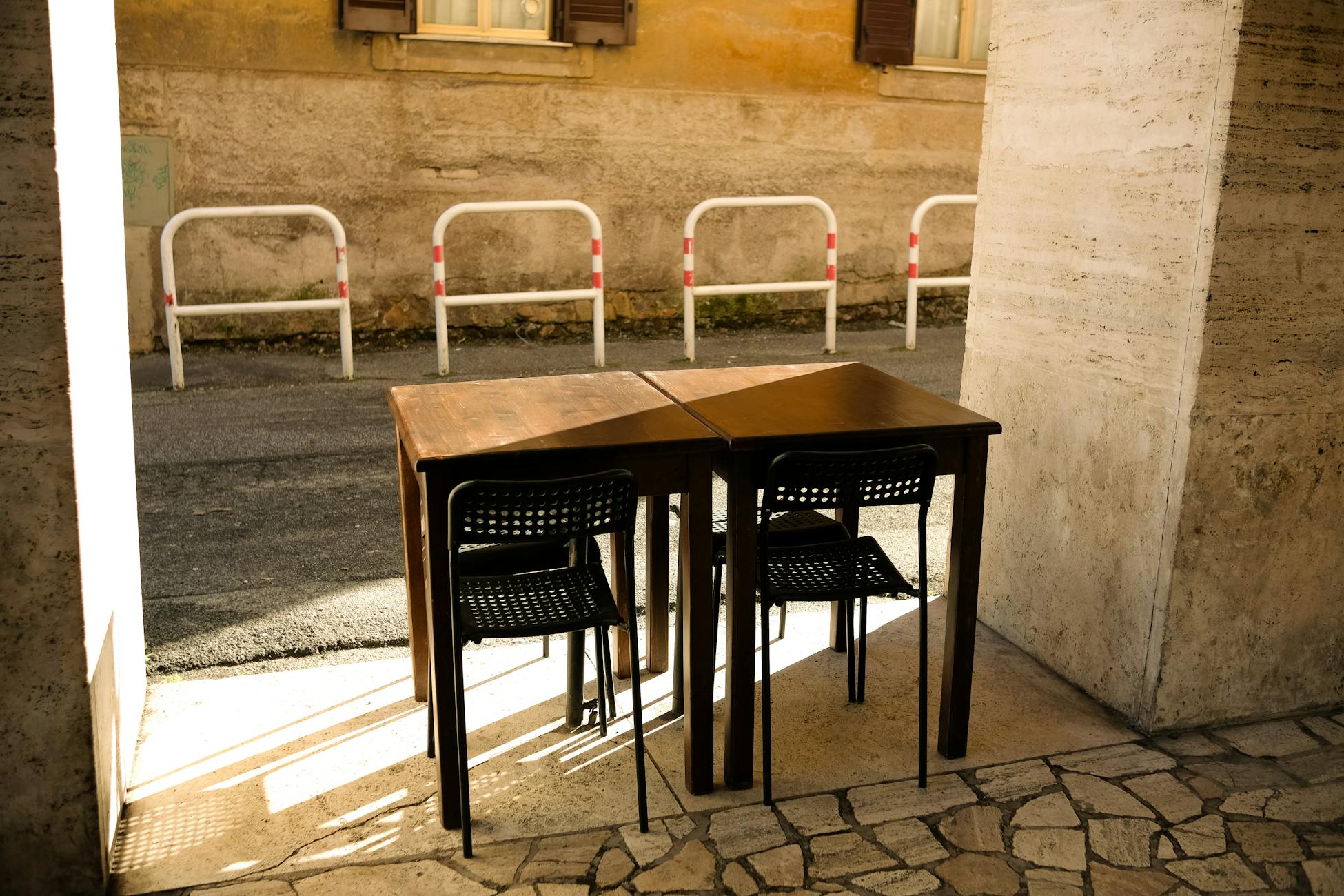 Outdoor table and chairs in a sunlit urban alleyway, casting long shadows.