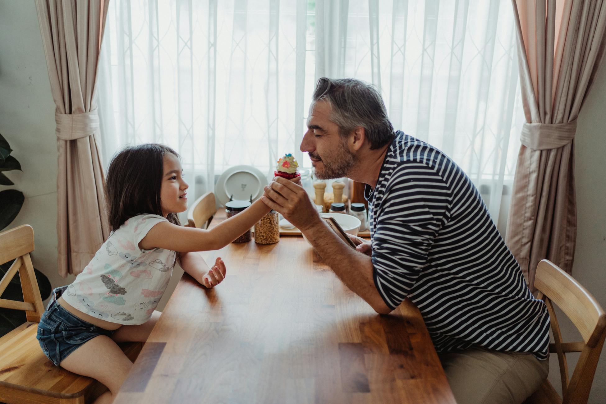A father and daughter share a special moment at the dining table with a cupcake.